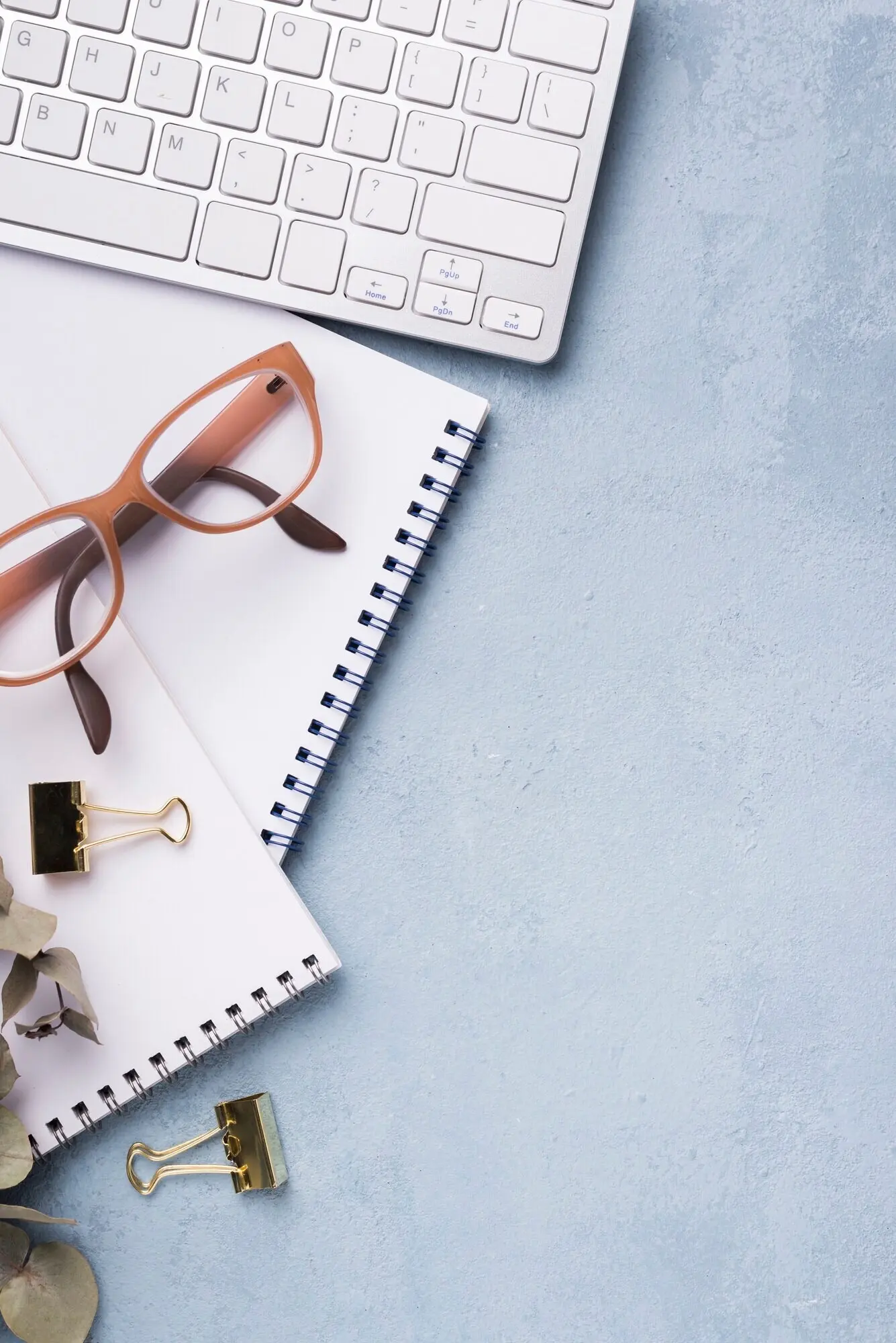 Draufsicht auf ein Notizbuch mit getrockneten Blättern und einer Brille auf einem Schreibtisch.
